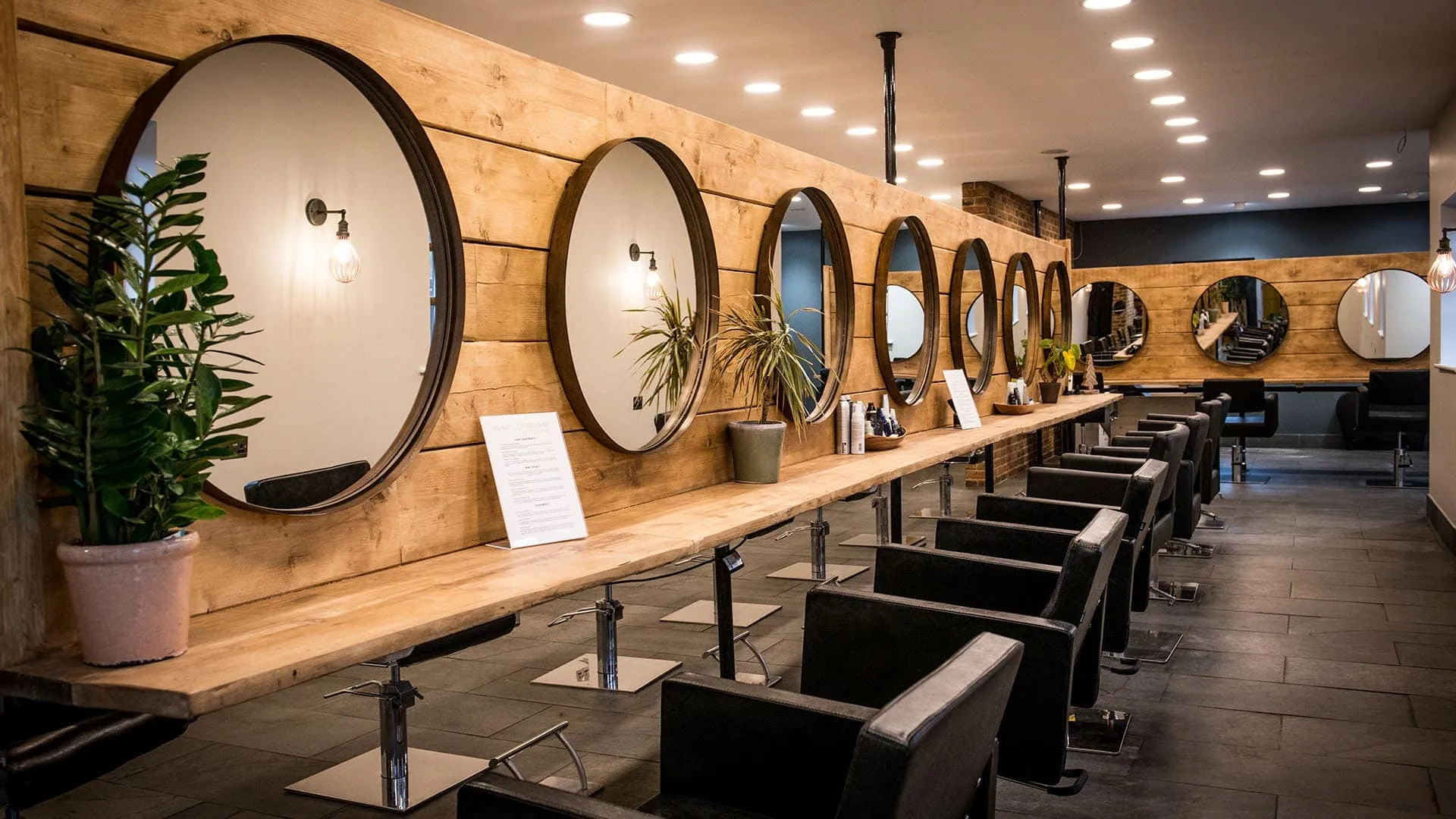 The Seckingtons salon: a long oak shelf, round bronze mirrors and black leather chairs